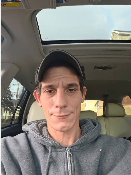 Man sitting inside a car, wearing cap.