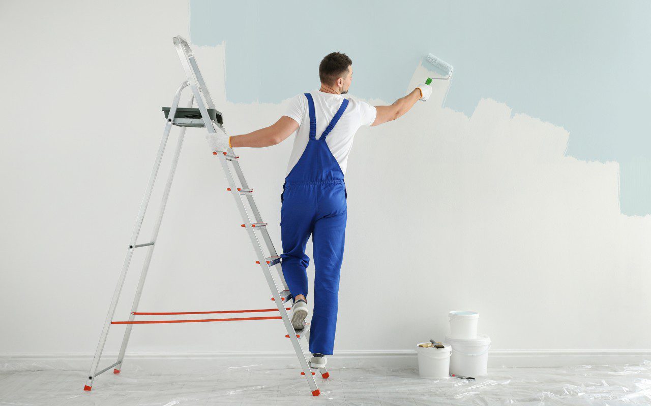 Painter on ladder applying light blue paint.